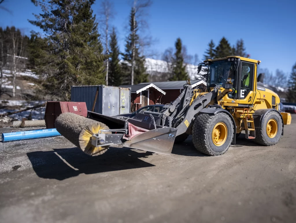 Hjullastare utrustad med sopvals för sopning av vägar och grönytor